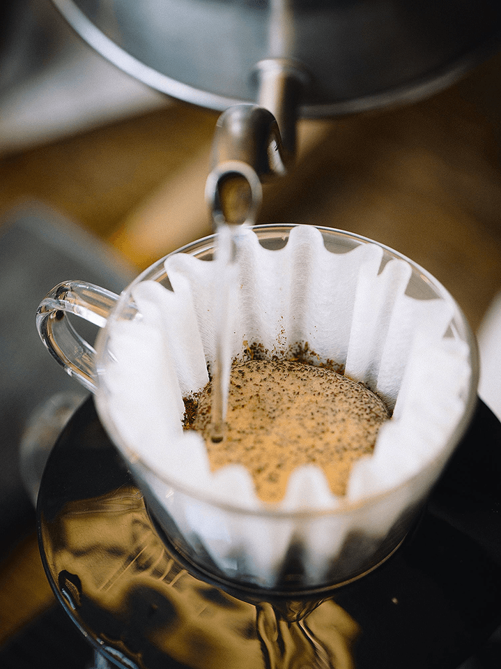 Water pouring from a kettle onto ground coffee in a paper filter.